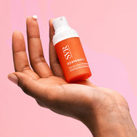 Hand holding an orange bottle with a white cap against a pink background